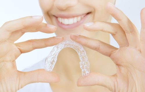 woman holding an invisalign retainer clear braces