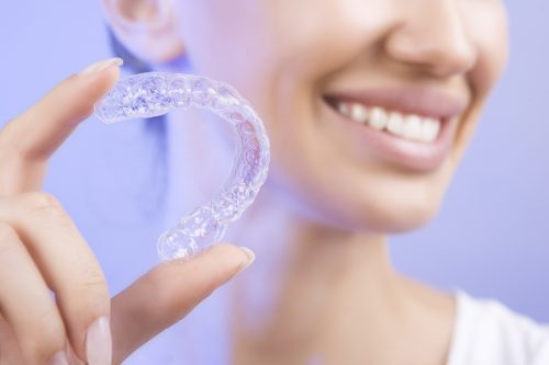 lady holding a clear braces invisalign retainer smiling with more confidence