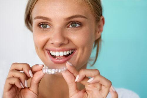a woman holding an invisalign clear aligner smiling and showing her straightened teeth