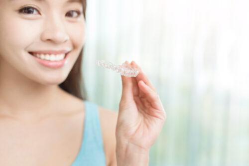 young lady professional holding an invislalign clear aligner to straighten her teeth